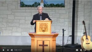 Man speaking at church podium with guitar