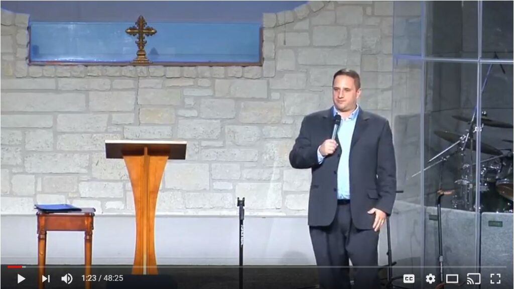 Man speaking on stage in a church setting.