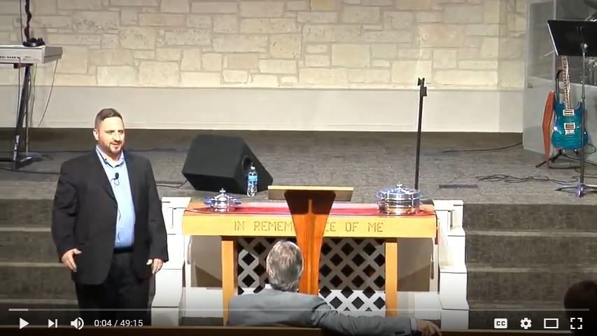 Man speaking at church service podium indoors.