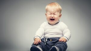 Crying baby in white shirt and pants.