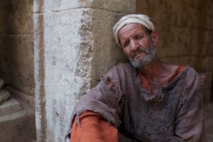 Elderly man resting against ancient stone wall