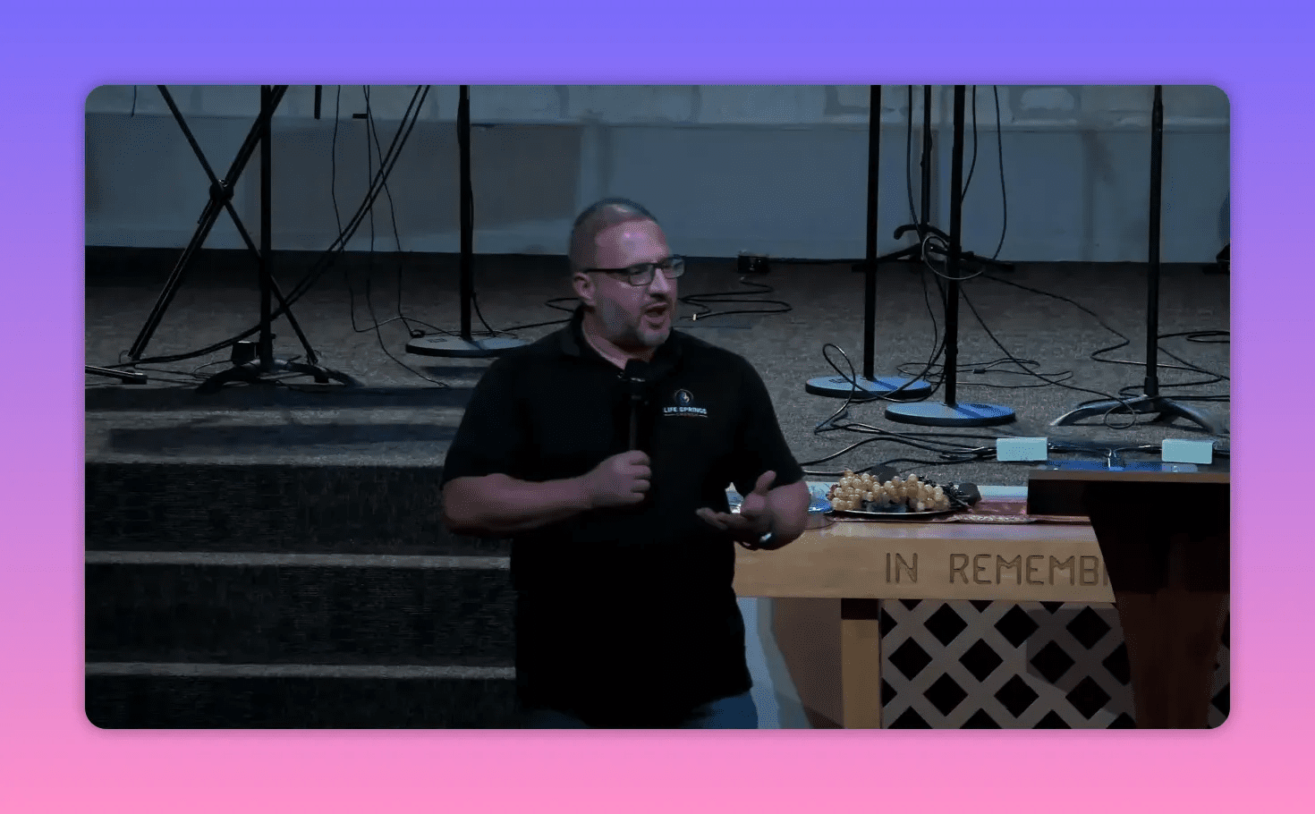 Clear frontal shot of a speaker on stage holding a microphone and gesturing, communion table and microphone stands visible behind