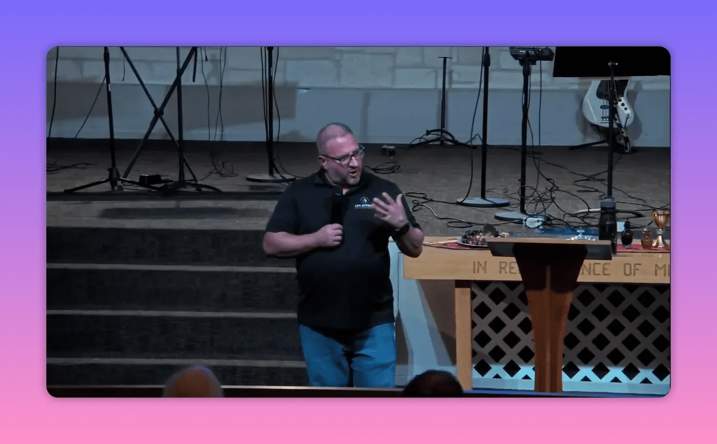Speaker on the front of the stage making an emphatic hand gesture while holding a microphone, lectern and communion table visible