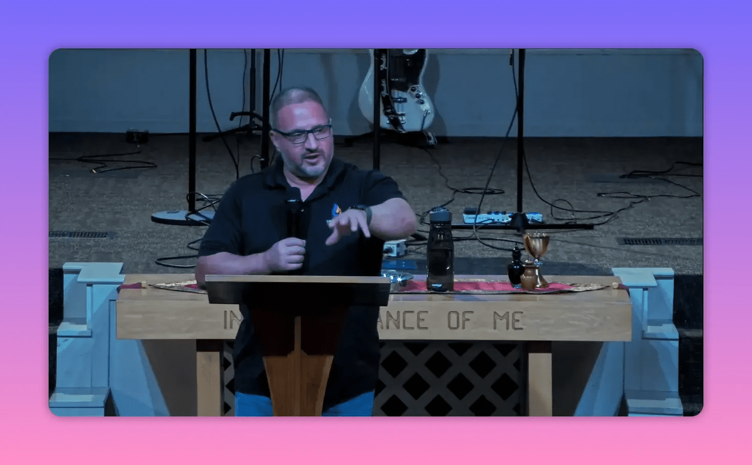 Speaker at a lectern extending a hand toward the congregation with the communion elements visible on the table beside him