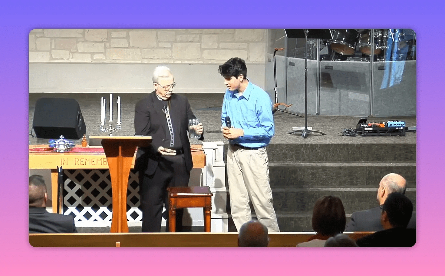 Pastor showing a glass jar to the congregation while a young man holds a microphone and watches