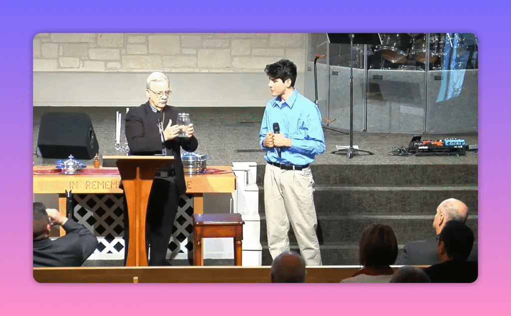 clear view of a speaker holding a mason jar on church stage with a young man beside him
