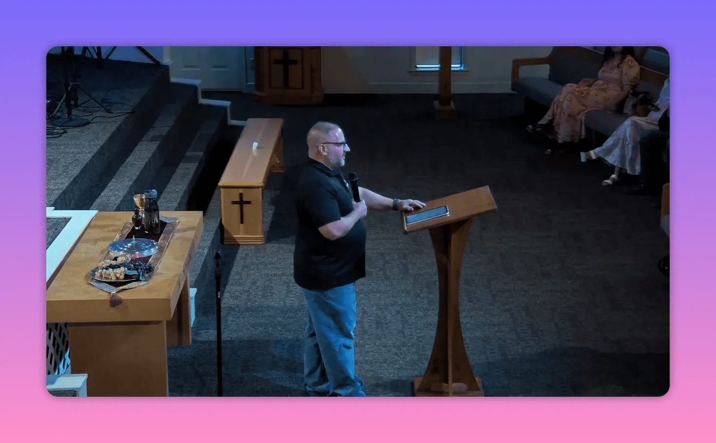 Pastor with one hand on a tablet and a microphone in the other, teaching from the lectern.