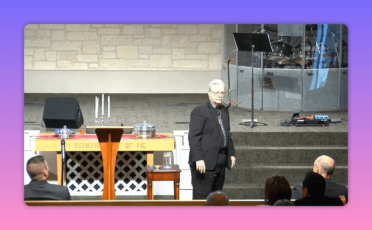 pastor standing beside a communion table and small jar on stage during a sermon