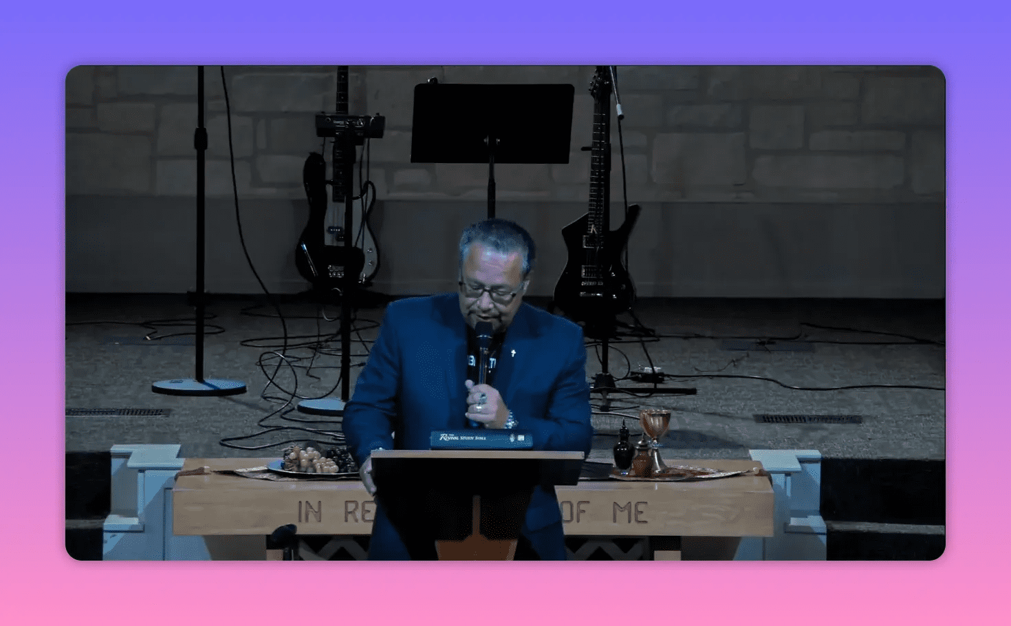 Speaker at a wooden pulpit with an open Bible and communion elements, speaking into a microphone.