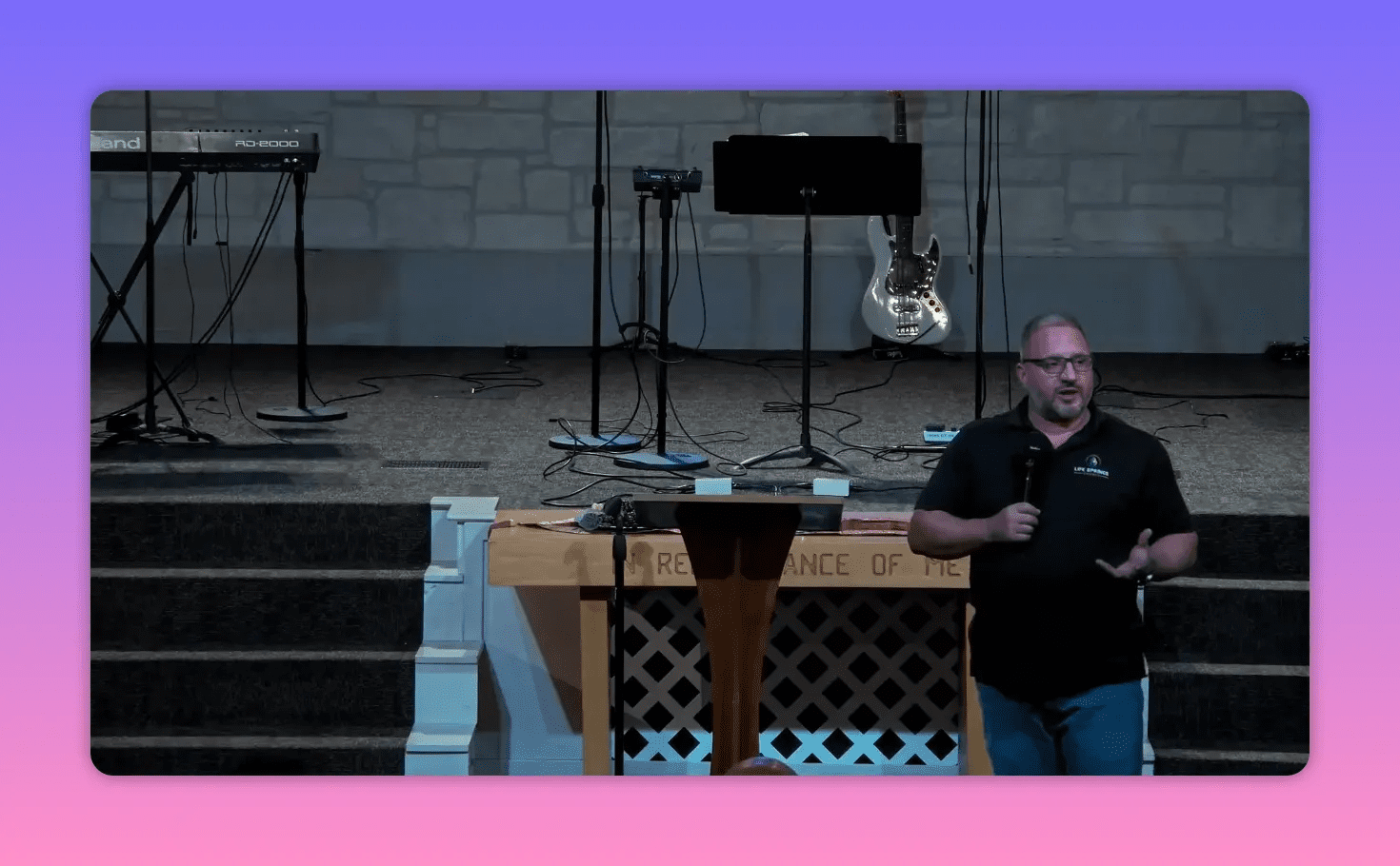 Centered shot of a speaker in front of the communion table and stairs, holding a microphone and making a hand gesture.