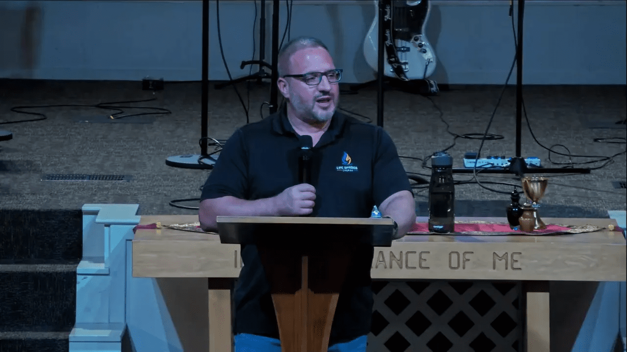 Church speaker at a lectern holding a microphone with the communion cup and elements on the table in front