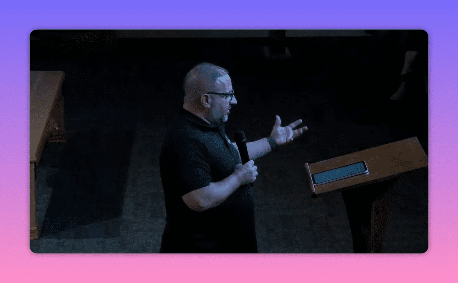 Side view of speaker gesturing with one hand while holding a microphone beside a lectern with a tablet on it