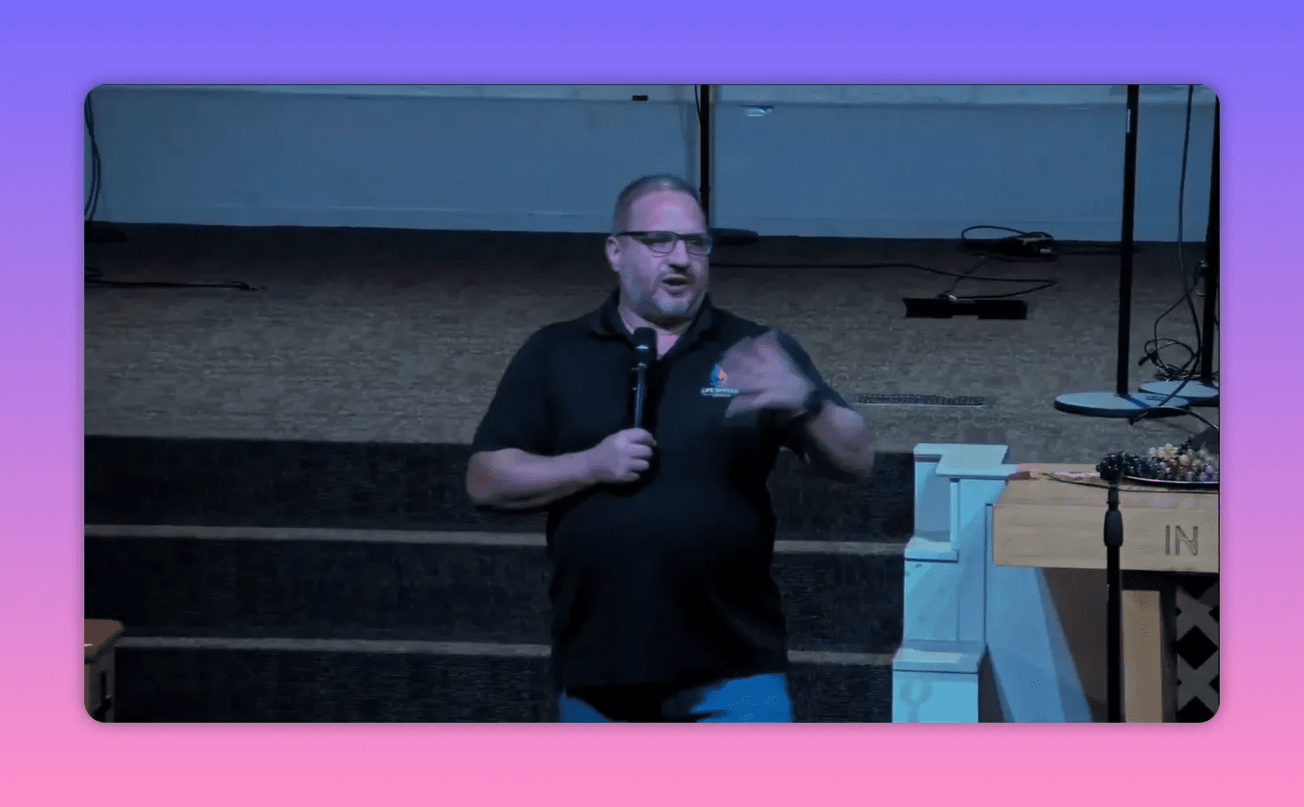 centered shot of speaker on stage gesturing while holding a microphone