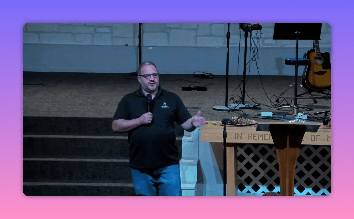clear image of speaker standing beside a communion table gesturing with one hand while holding a microphone
