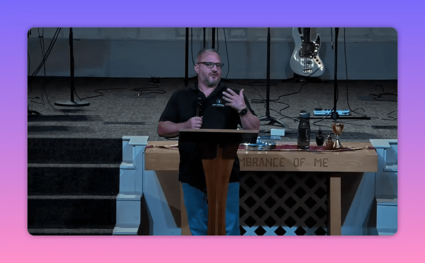 speaker gesturing at pulpit with communion table and guitar in background