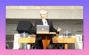 speaker using open hand gestures at pulpit with communion table foreground