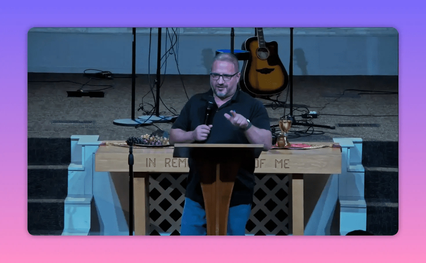Speaker pointing and speaking behind a lectern with communion table and guitar in the background