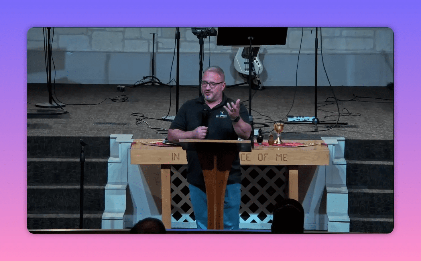 Speaker beside the pulpit smiling and making an open-handed gesture while addressing the audience, communion table visible