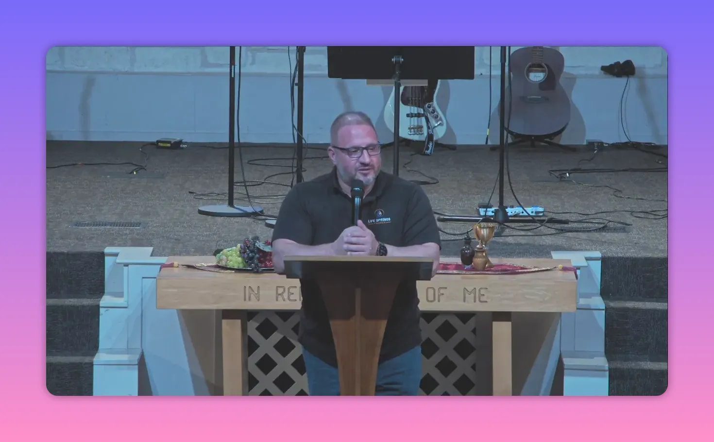 Wide shot of a pastor speaking at a lectern with communion elements on the table and musical instruments behind him.