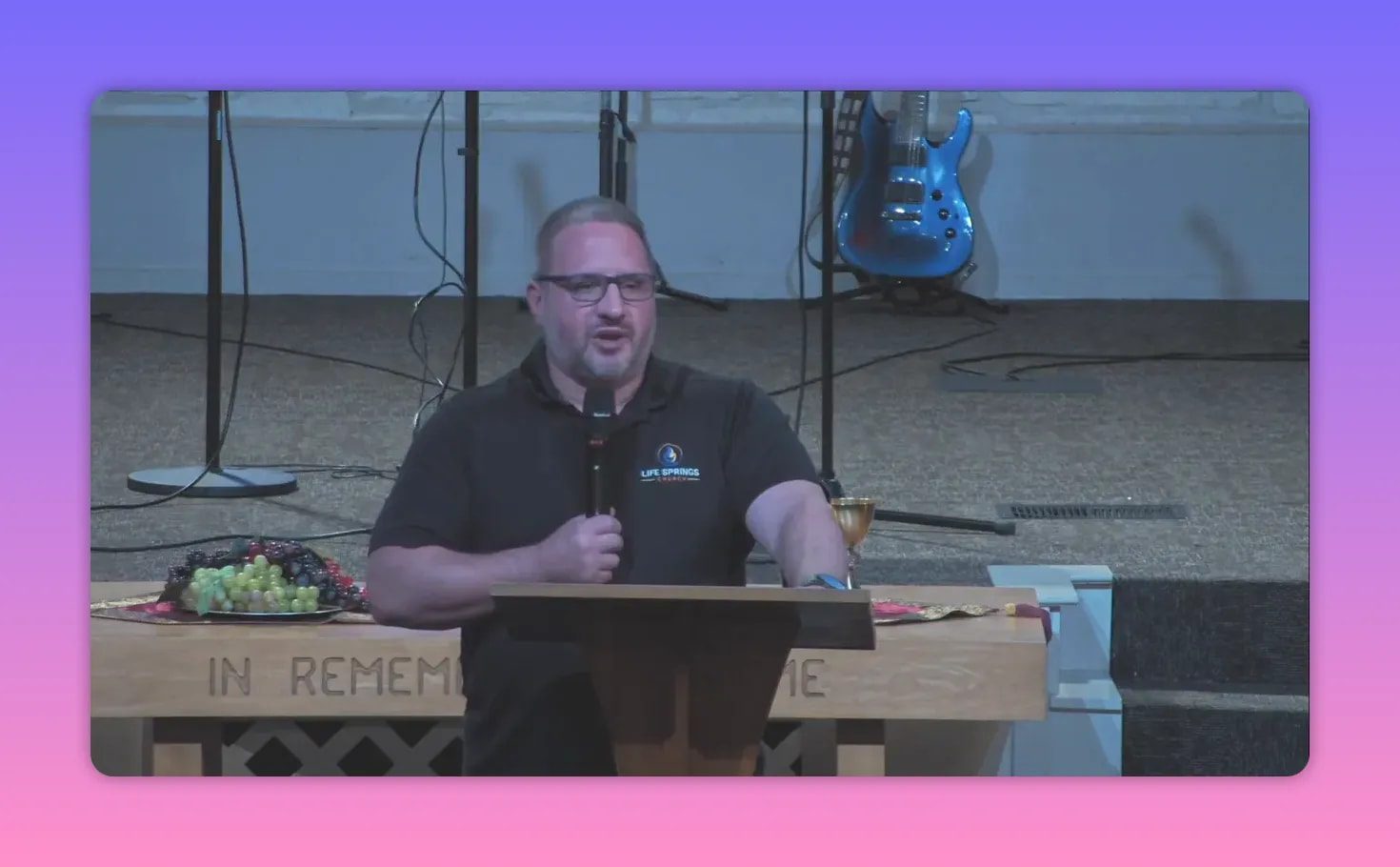 Front-facing speaker at a lectern next to a communion table with a plate of fruit and a chalice