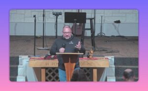 speaker gesturing at pulpit in church sanctuary with communion table and inscription visible