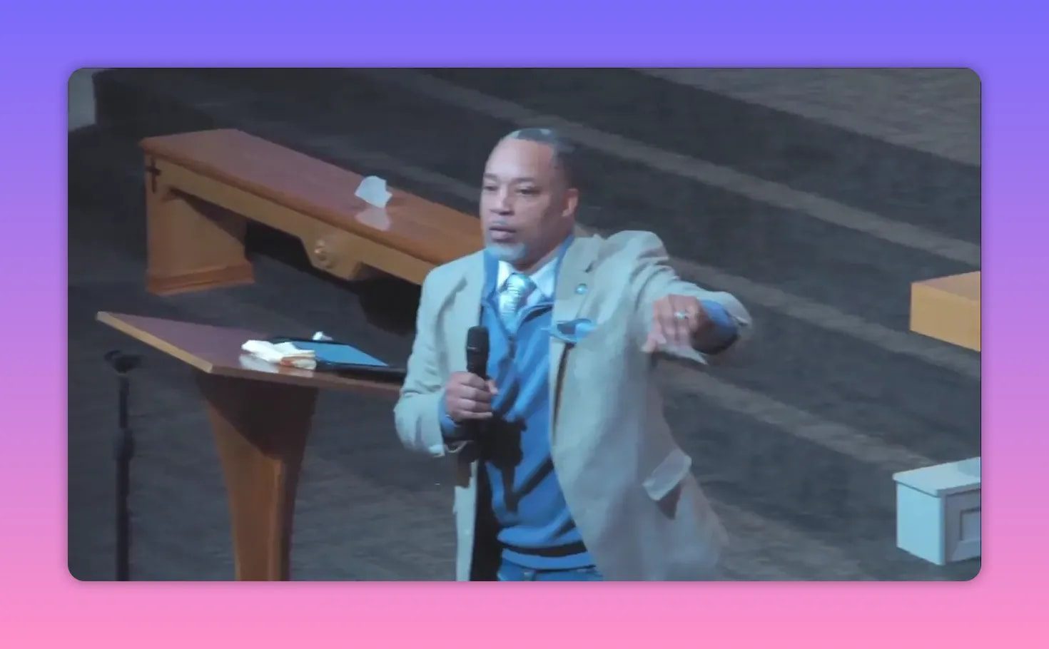 Speaker holding a microphone and pointing outward toward the congregation with pulpit and steps behind