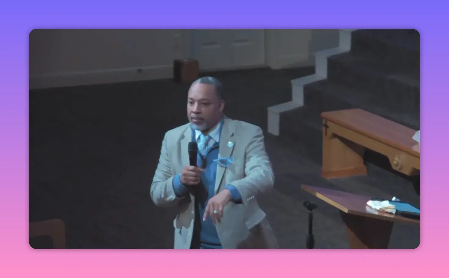 Preacher on stage holding a microphone with a calm, prayerful expression