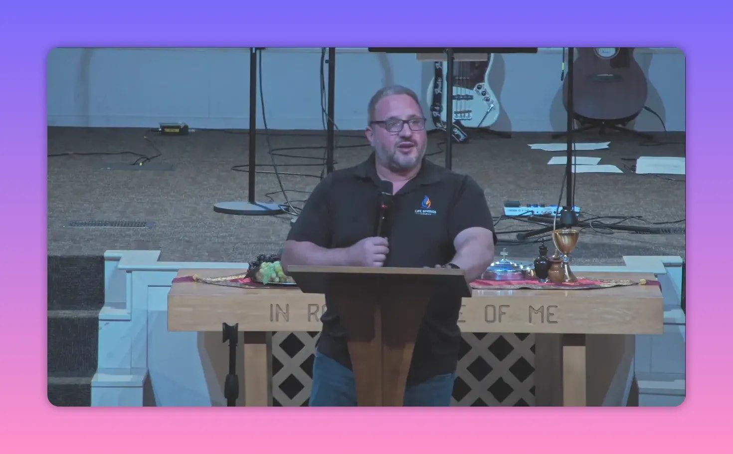 Minister speaking from a pulpit with communion tray and instruments in the background