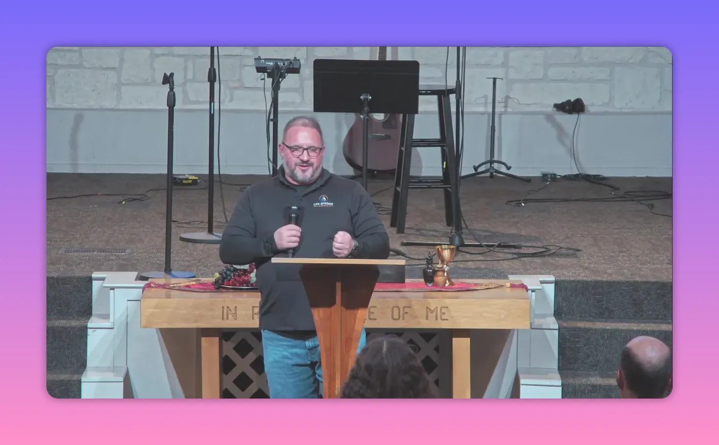 speaker at church lectern with communion cup and 'In Remembrance of Me' on the altar clearly visible