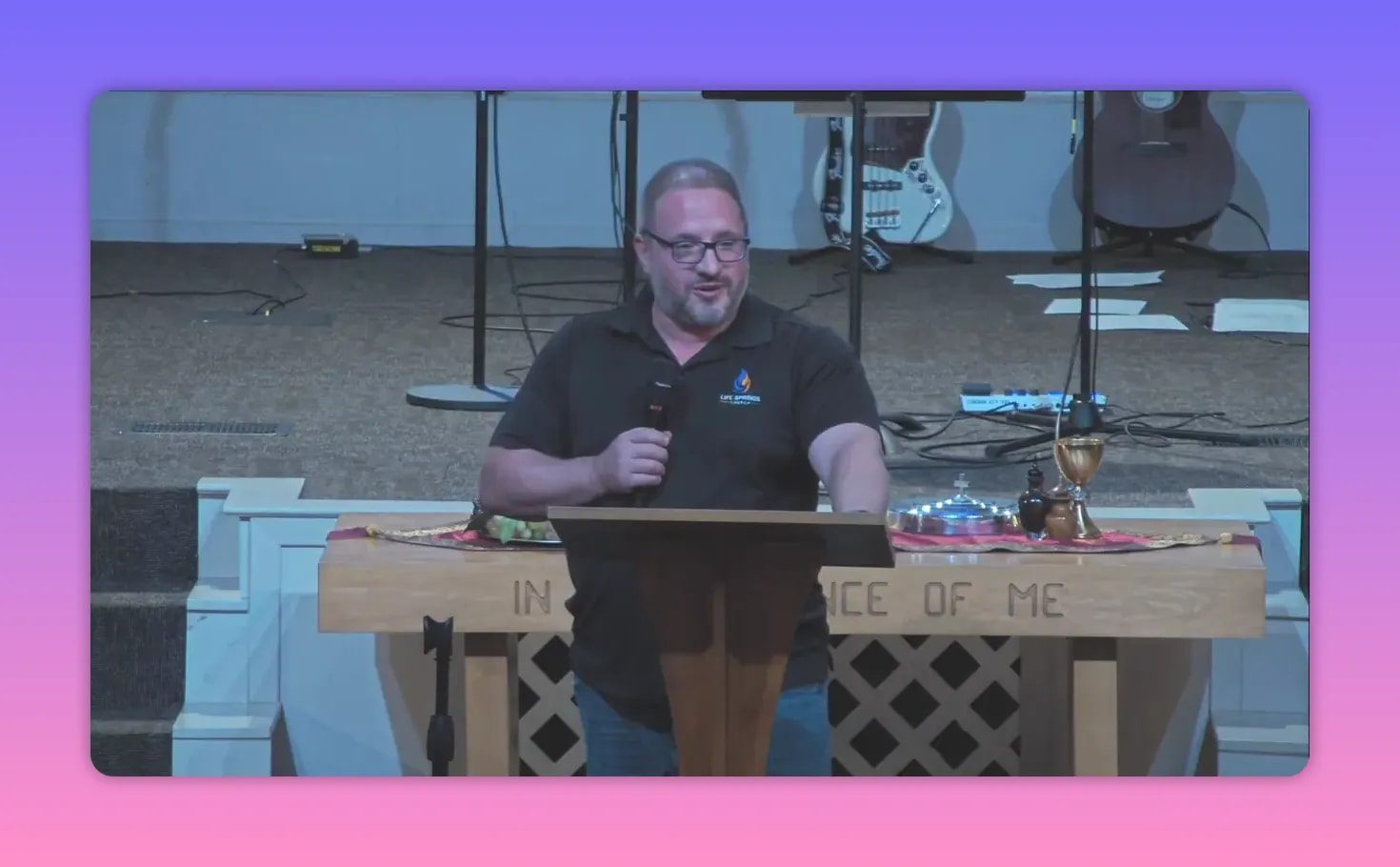 Centered view of a pastor at a wooden pulpit with communion elements and instruments in the background