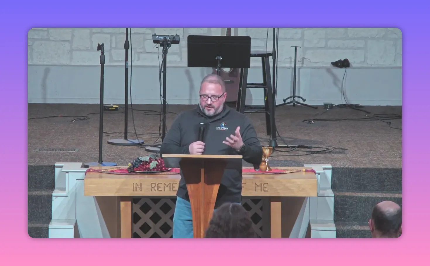 Speaker at pulpit with open hand gesture, communion elements on the table behind him