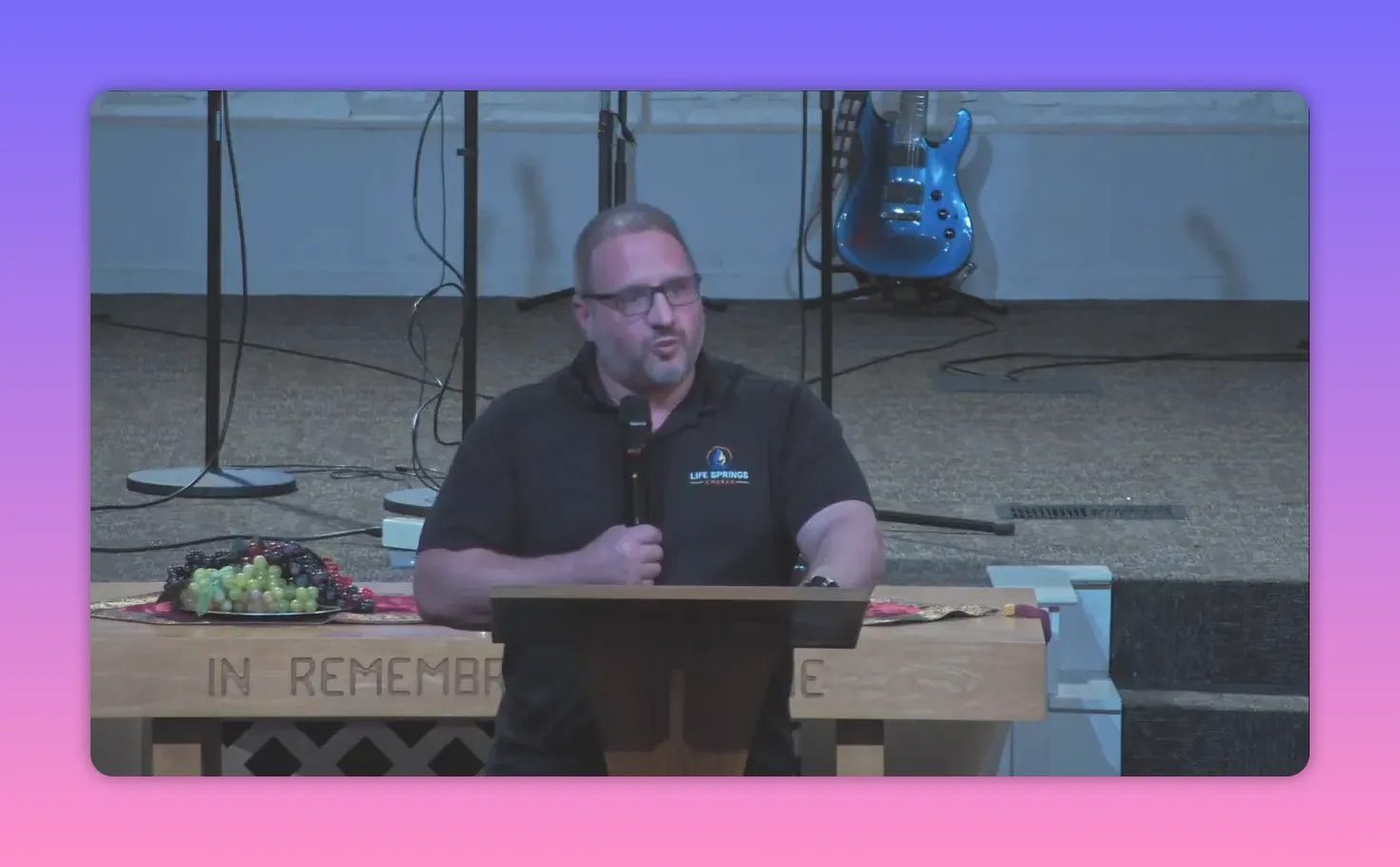 speaker at lectern making a gesture while speaking, communion table with fruit visible in foreground
