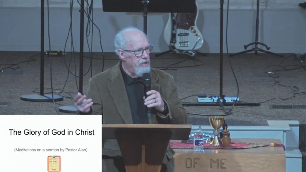 Speaker gesturing at a pulpit while a slide titled 'The Glory of God in Christ' appears on screen