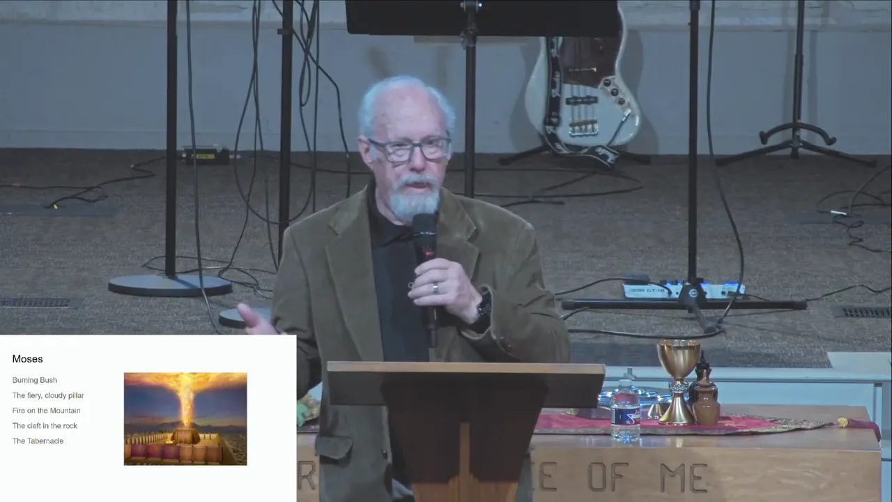 Front view of the presenter at the lectern with a clear Moses slide showing a burning-pillar image and bullet points