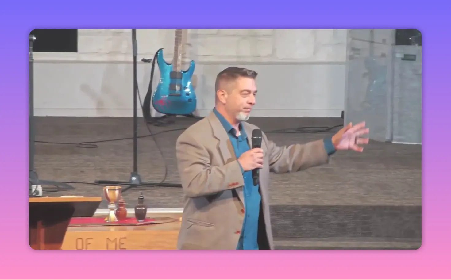 Speaker on stage holding a microphone and extending an open hand outward as if inviting conversation.