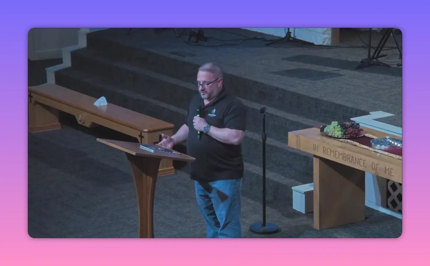 Pastor reading from notes at a pulpit beside a communion table engraved 'In remembrance of me'