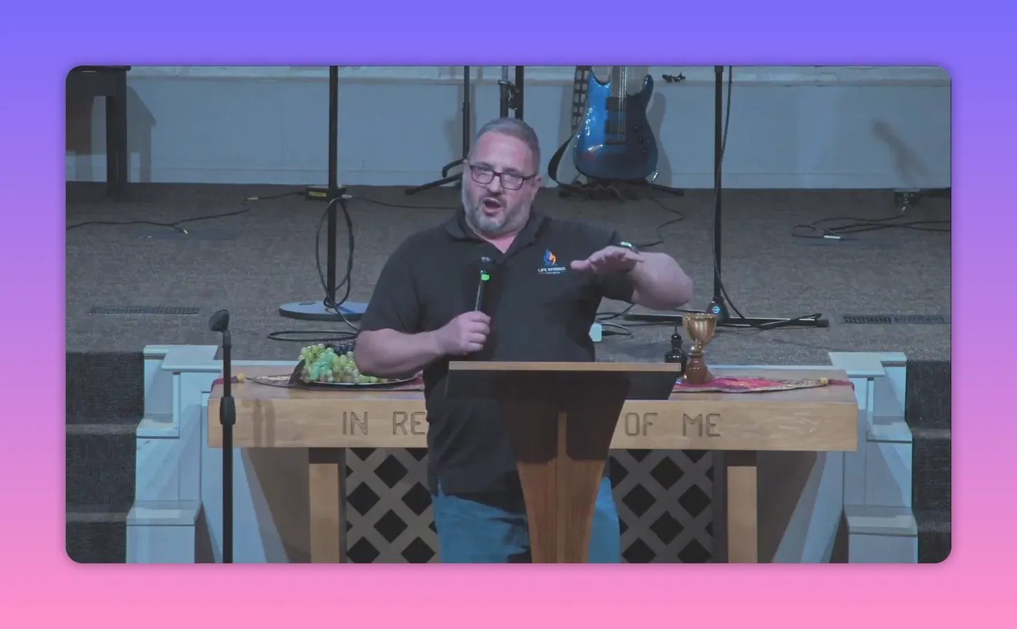 Pastor at a wooden pulpit with communion chalice and tray of grapes on the table behind him