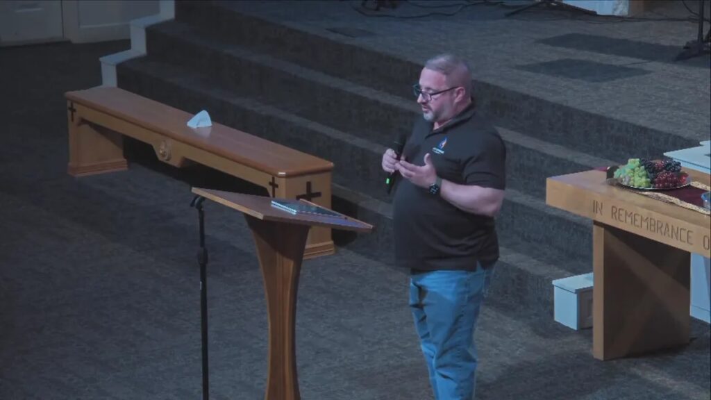 Speaker at a church lectern on stage with communion table and steps visible behind him