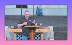 clear framed speaker at lectern with communion elements and guitar behind