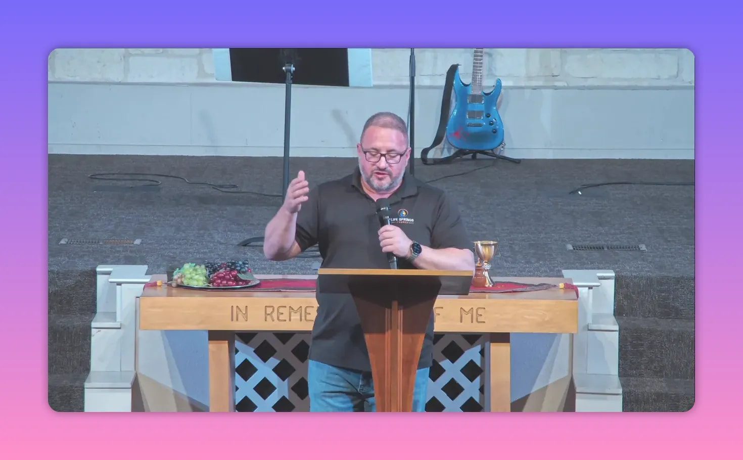 Speaker at lectern making an open hand gesture, microphone in hand, communion plate and cup visible