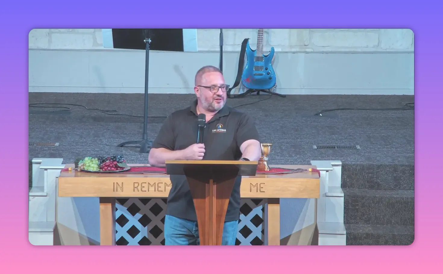 speaker standing at lectern looking to the side with communion table and guitar behind