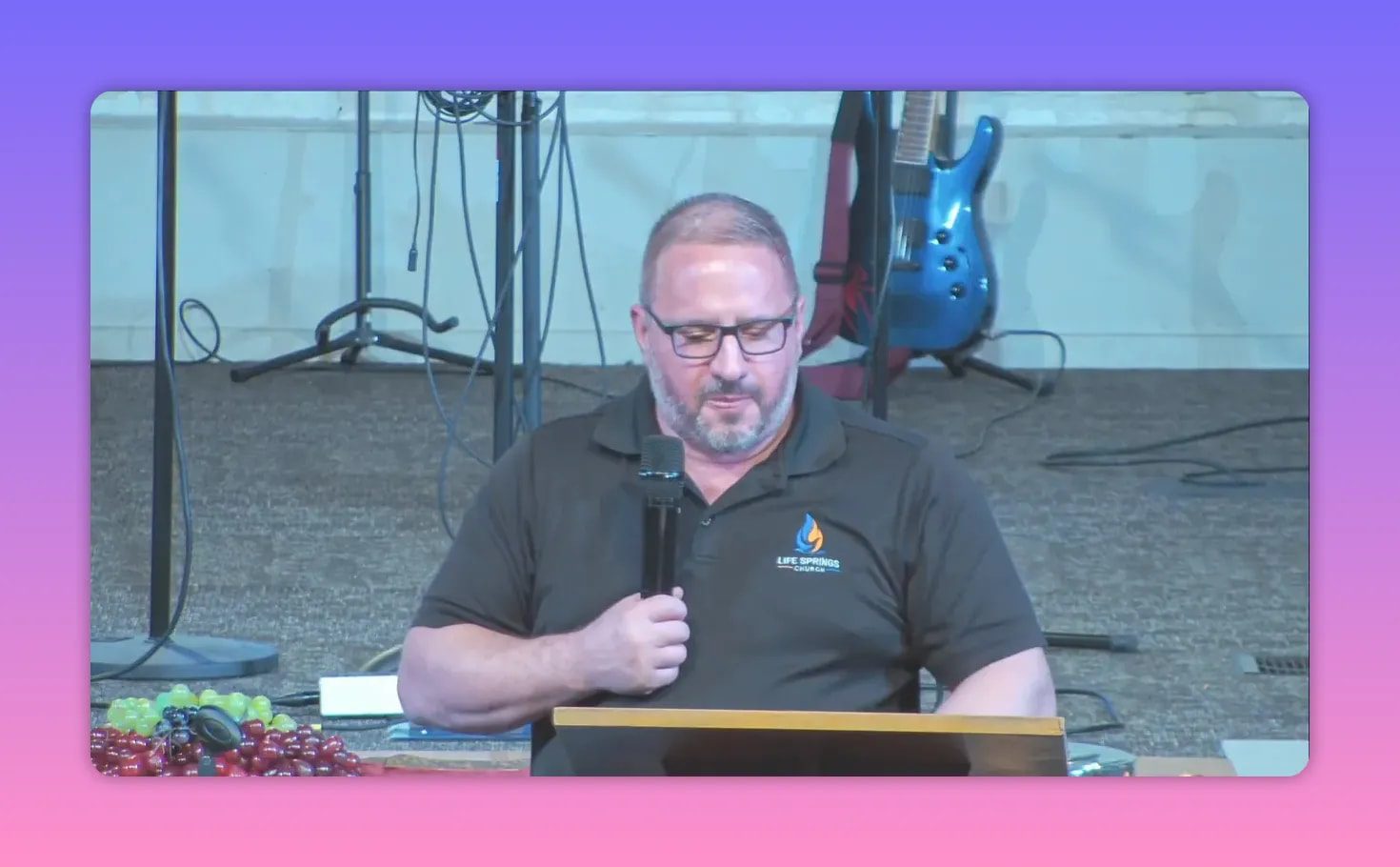 Church speaker at a lectern holding a microphone while speaking with a calm expression