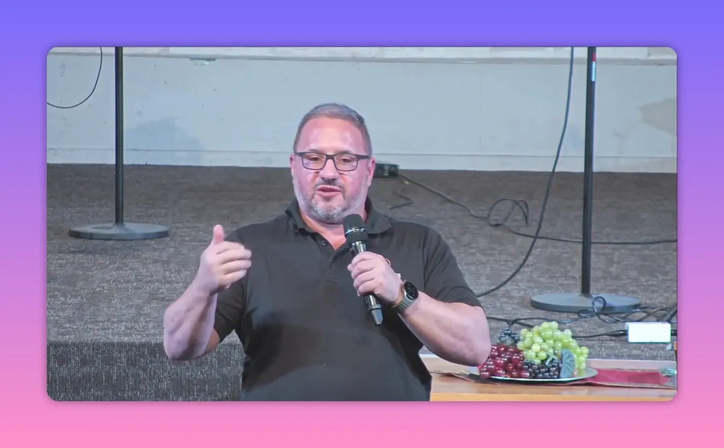 Pastor speaking at an outdoor podium in the rain holding a microphone and pointing while teaching