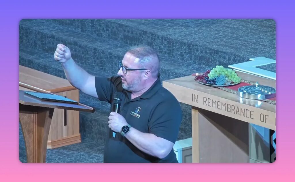 Speaker raising one arm and holding a microphone during a rainy sermon at a church stage.